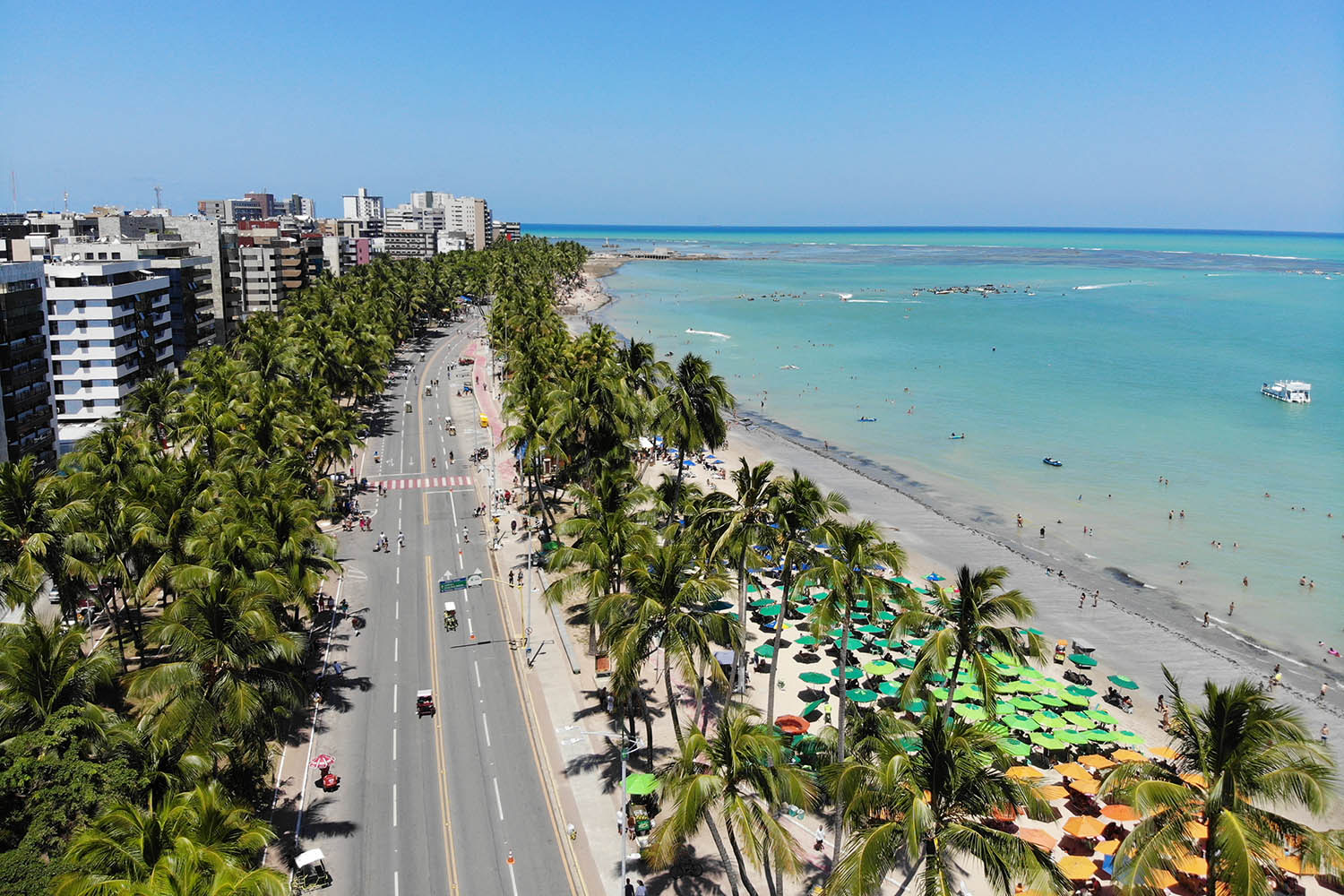 Vista aérea da orla de Maceió com praia, recifes e edifícios